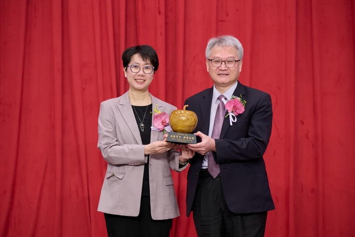 財團法人中山醫學大學董事長周英香(左)致贈校園桃花心木雕製的蘋果紀念藝品予卸任校長黃建寧，感謝其深耕教育、培育人才，為中山醫大奠定穩固發展基礎。圖片